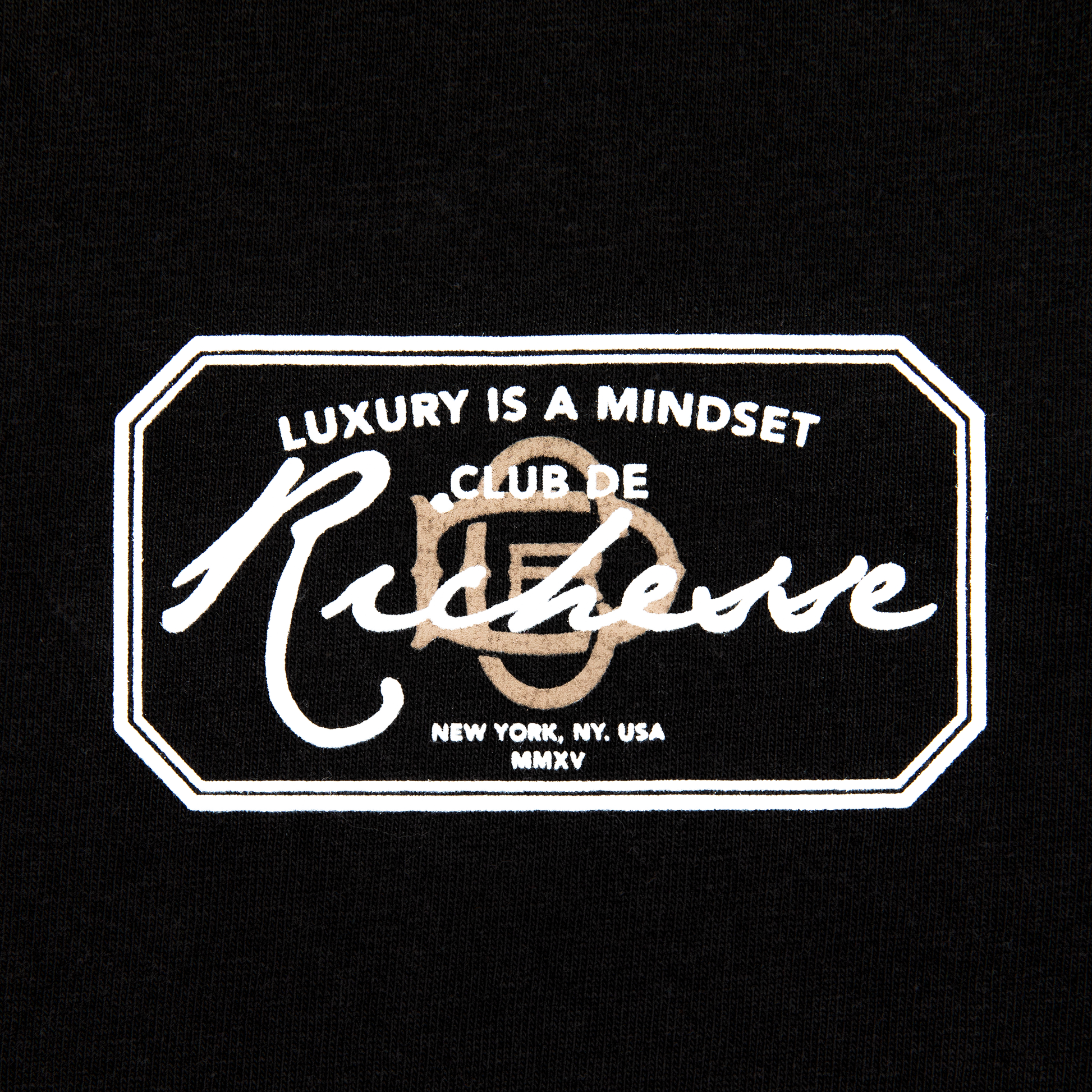 Chest close up view of a black tee with refined embroidery detail on the sleeve and screen-printed details on the front and back, this tee delivers a balance of comfort, structure, and everyday wearability.